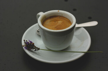 Cup of coffee with a saucer lying next to a lavender flower and standing on the table 