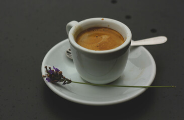 Cup of coffee with a saucer lying next to a lavender flower and standing on the table 