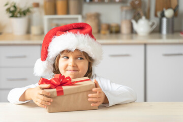 Cute child opens Christmas box with a gift at home. Happy Little girl in a Christmas hat Santa...