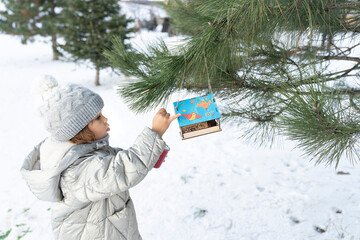 Child girl feeding birds in winter. Bird feeder in snowy tree, helping birds during cold season,...