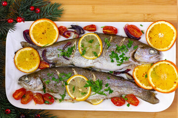 Pieczone pstrągi z cytrusami i pomidorkami na białym półmisku otoczone gałązkami świerku