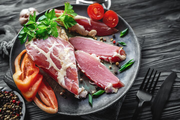 large piece of dried meat in a thin mesh of internal fat. A piece of fresh smoked meat lies on spinach leaves. Venison fillet steak natural with tomatoes close-up