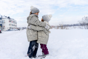 Funny girls hugging in the winter in the snow. Happy sisters play snow games. Children Friends are happy to be together on a cold winter day