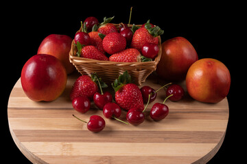 Basket with strawberries and cherries and nectarines. Bamboo board. black background.