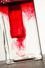 Seringue injectant un produit rouge dans un bocal