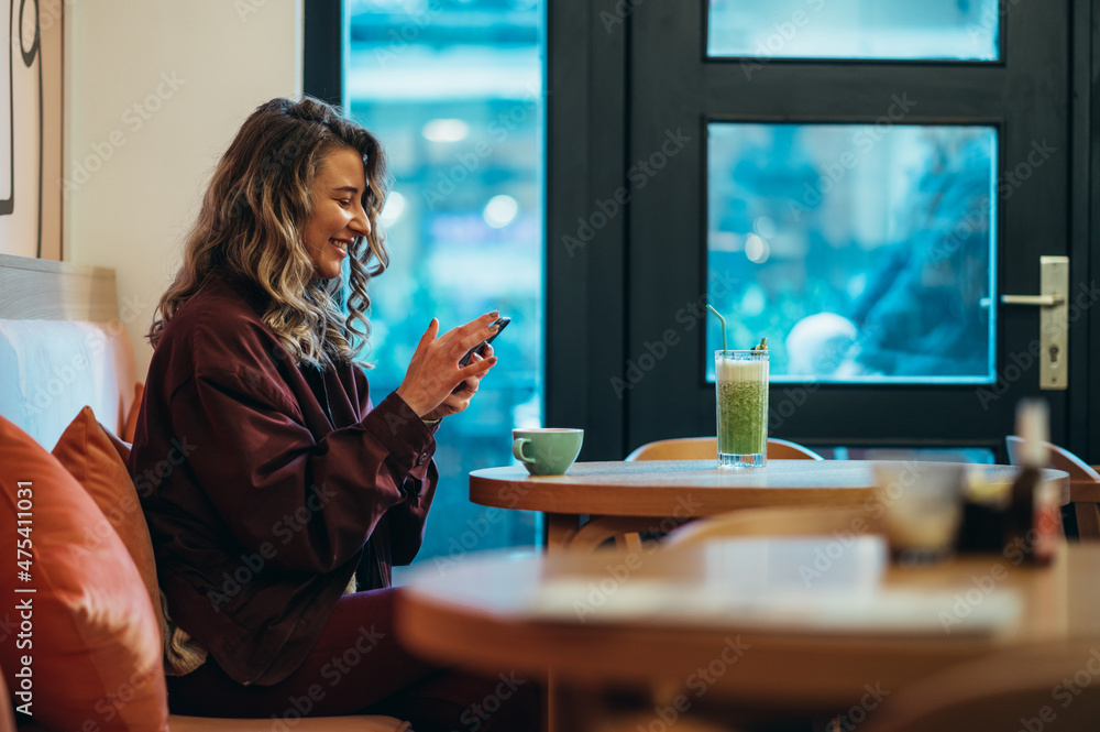 Wall mural beautiful young woman drinking coffee and using smartphone in a cafe