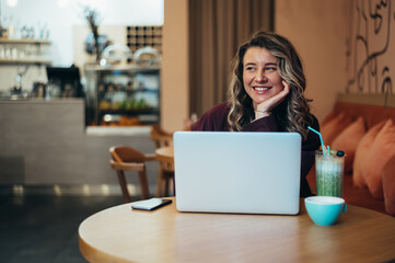 Beautiful young woman drinking coffee and working on her laptop in a cafe