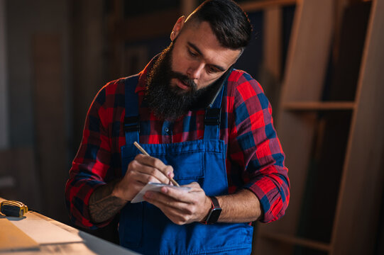 Young male carpenter working in workshop and using smartphone