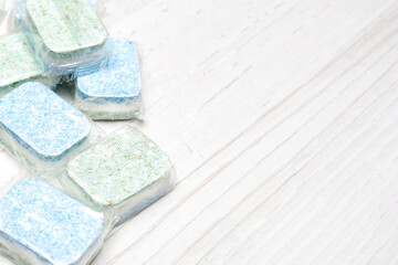 Green and blue dishwasher tablets in water-soluble packaging close up on the table with copy space