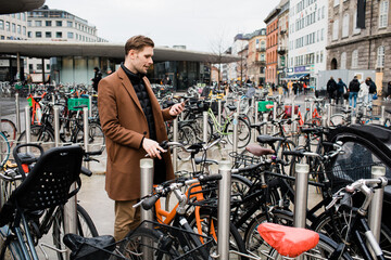 Young man unlocks bicycle with his mobile phone. Electric bicycle new way city mobility. Green...