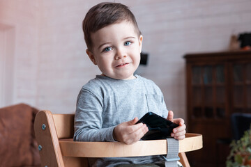Fototapeta na wymiar Cute little toddler boy playing with smartphone Healthy baby touching mobile phone with fingers, looking cartoons and having fun with educational apps. Child at home