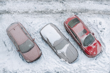 Top aerial view of apartment office building parking lot with many cars covered by snow stucked after heavy blizzard snowfall winter day. Snowdrifts and freezed vehicles. Extreme weather conditions