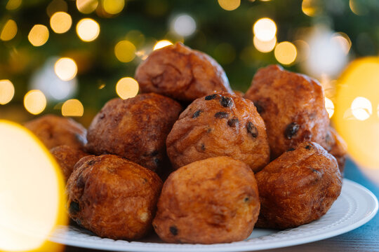 'Oliebollen', traditional Dutch pastry for New Year's Eve with sparkles. oil dumpling or fritter with sugar powder on top. Christmas tree lights bokeh on background. Typical food. Selective focus