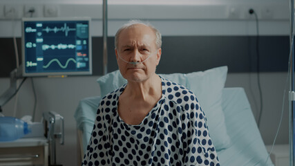 Portrait of elder patient with nasal oxygen tube standing on bed in hospital ward at medical clinic. Sick old man with oximeter connected at heart rate monitor to check progress - obrazy, fototapety, plakaty