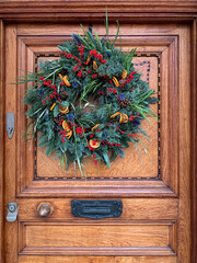 Christmas mood: festive christmasy themed winter natural wreath on a wooden door. Elegant charming wreath decorated oranges, berries, herbs, fir tree, pine cones