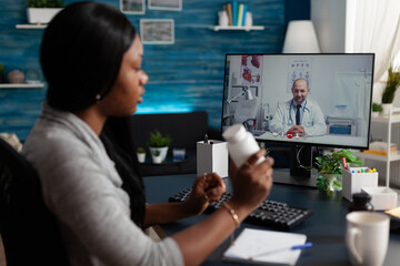 African american patient using video call to talk to doctor on computer, asking for medical advice with bottles of pills. Woman talking to medic about healthcare on telemedicine conference