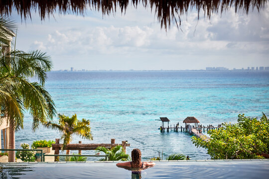 beautiful young woman swimming in an infinity pool next to the ocean