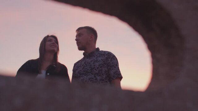 Portrait of a man and a woman in a hole in a concrete fence. They look around, orientation on the terrain, search for an object. The red tint of the sky.