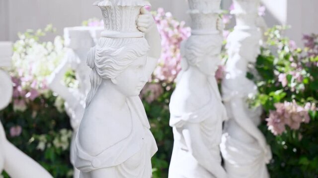 Close-up of female statues in marble. A row of beautiful antique sculptures against the background of flowering trees