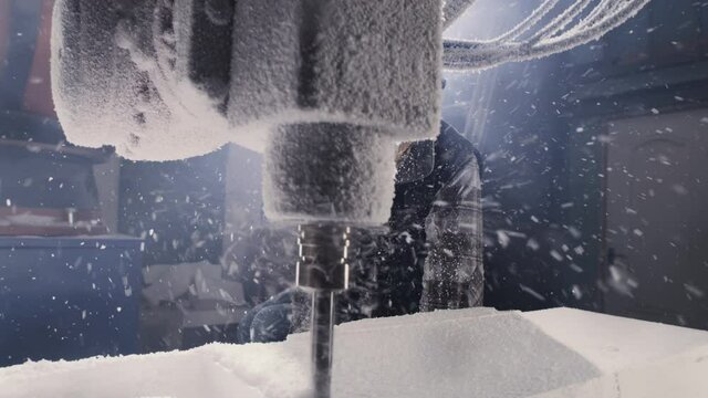 Zoom out view of man in face shield and respirator watching robotic arm milling machine cutting polymer block in professional workshop