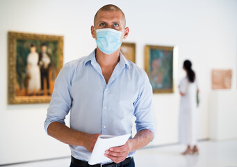 Portrait of European adult man in mask standing in gallery and watching exposition