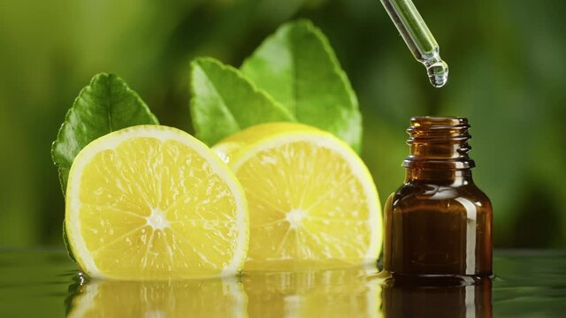 Dripping lemon juice from pipette into bottle close-up, vitamin oil. Making aroma serum on green background. Dropping liquid citrus extract, skincare routine, treatment spa. Traditional medicine. 