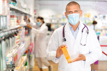 Male pharmacist in medical mask offers medicine while standing in the trading floor of a pharmacy