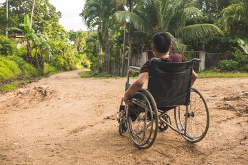 An anonymous paraplegic man on his old wheelchair staring far away. Traveling on a dirt road at a...