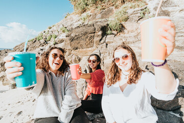 Diverse group of young adult friends people in casual outfit at the beach talking, drinking and...