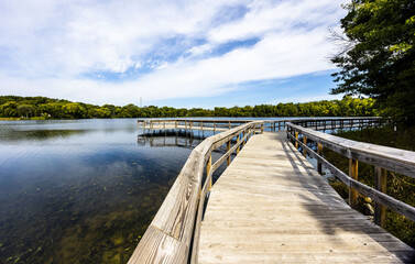 Wooden bridge over the reflective clean lake Carver surrounded by dense trees in Minnesota