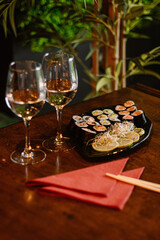 Obraz na płótnie Canvas Sushi set na talerzu w restauracji z imbirem i wasabi, kieliszki wina, kolacja dla dwoch, obiad