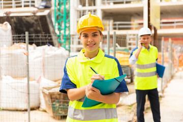 European woman engineer filling documentation while standing in construction site. Her male...