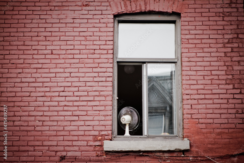 Poster fan on a windowsill of an open window of a brick building