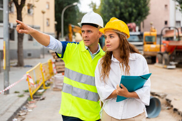 Contractor working on a construction site shows something to a young woman engineer controlling the progress of work, ..pointing it out