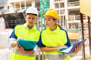 Two builders in uniform planning their work in construction plant. Woman using laptop, man holding...