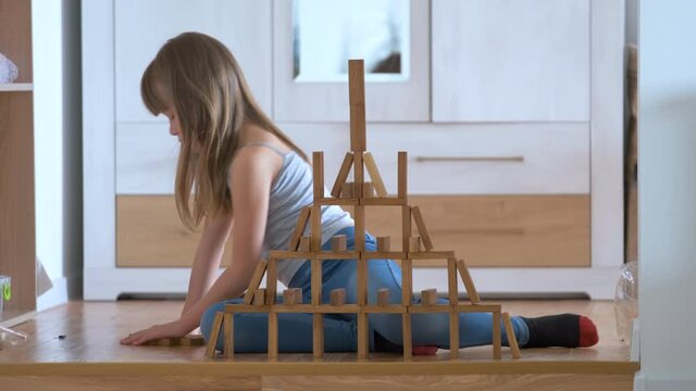 Happy child girl playing game stacking wooden toy blocks in high pile structure. Hand movement control and building computational skills concept