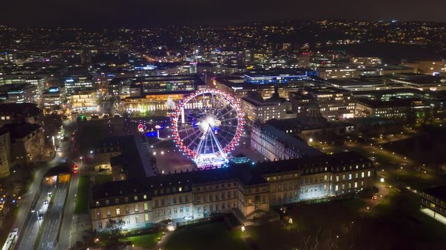 Moving aerial night time lapse in 4k of downtown skyline in the city of Stuttgart, Germany with Schlossplatz, the Länd ferris wheel and christmas market.