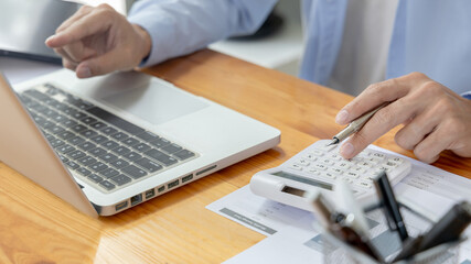 Financial or accounting professionals use a laptop to analyze the company's revenue-expenses graph to prepare for presentation to the chief executive and partner, Calculate data with a calculator.