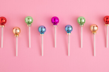 Creative concept with Christmas baubles like a lollipops on a pastel pink background. Minimal New year candy concept