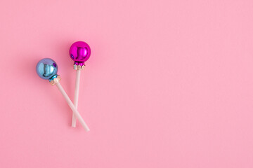 Creative concept with Christmas baubles like a lollipops on a pastel pink background. Minimal New year candy concept