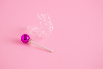 Creative concept with colorful Christmas baubles like a lollipops on a pastel pink background. Minimal New year candy concept