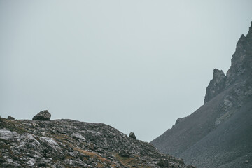 Atmospheric highlands landscape with narrow mountain valley and sharp rocks on steep slope under gray sky. Bleak mountain scenery with pointed rockies on mountainside and glen in overcast weather.