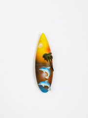 Magnetic Souvenir from Egypt, Thailand, Sri Lanka or Bali. Surfboard with sea, dolphins and palms on white fridge background. Tropical, surfing travel concept. Top view, flat lay, vertical, close up