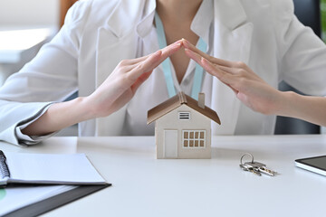 Female insurance agent hand protecting house model. Insurance or loan real estate concept.