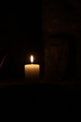 A candle burns against the background of masonry in the dark. Front view.