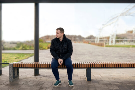 man sitting on bus stop and waiting for public transport