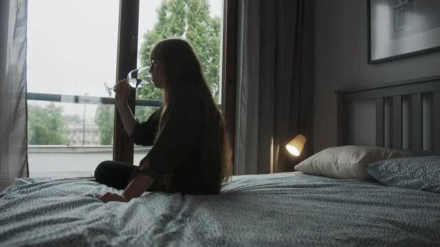 woman taking a sip from her white wine while sitting in her bedroom, silhouette slow-motion shot