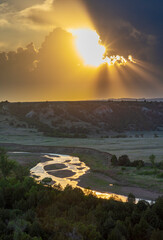 Setting sun rays poke through thunderstorm clouds above the Little Missouri River in the Little...