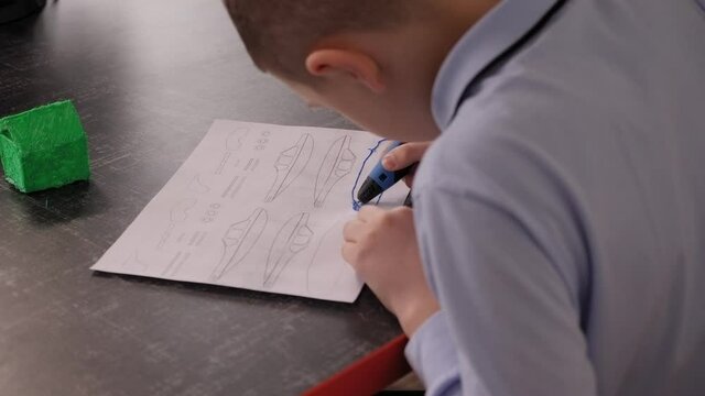 Close-up of child creates a new 3D object using a 3D pen from a robotics school. A boy draws details of a boat with a 3d pen in a modern computer school. Technical development of children.