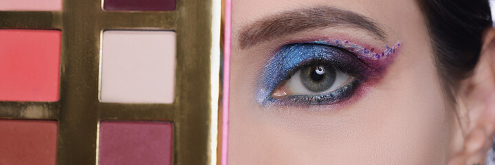 Woman with evening make-up holds eye shadow palette closeup